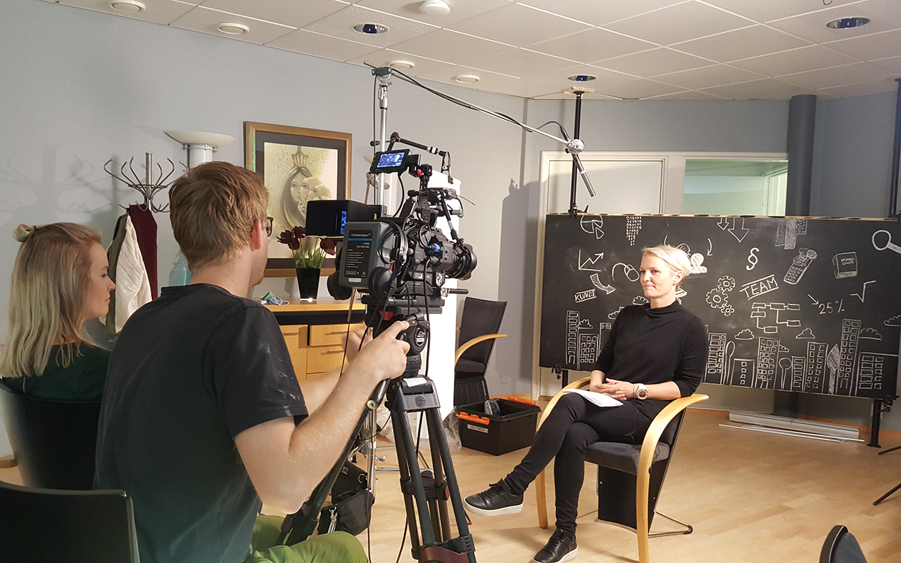 Kristin foran kamera blir intervjuet av Tine, begge ansatt i Økonomihuset på Hønefoss. Marius fra MG Film er produsent